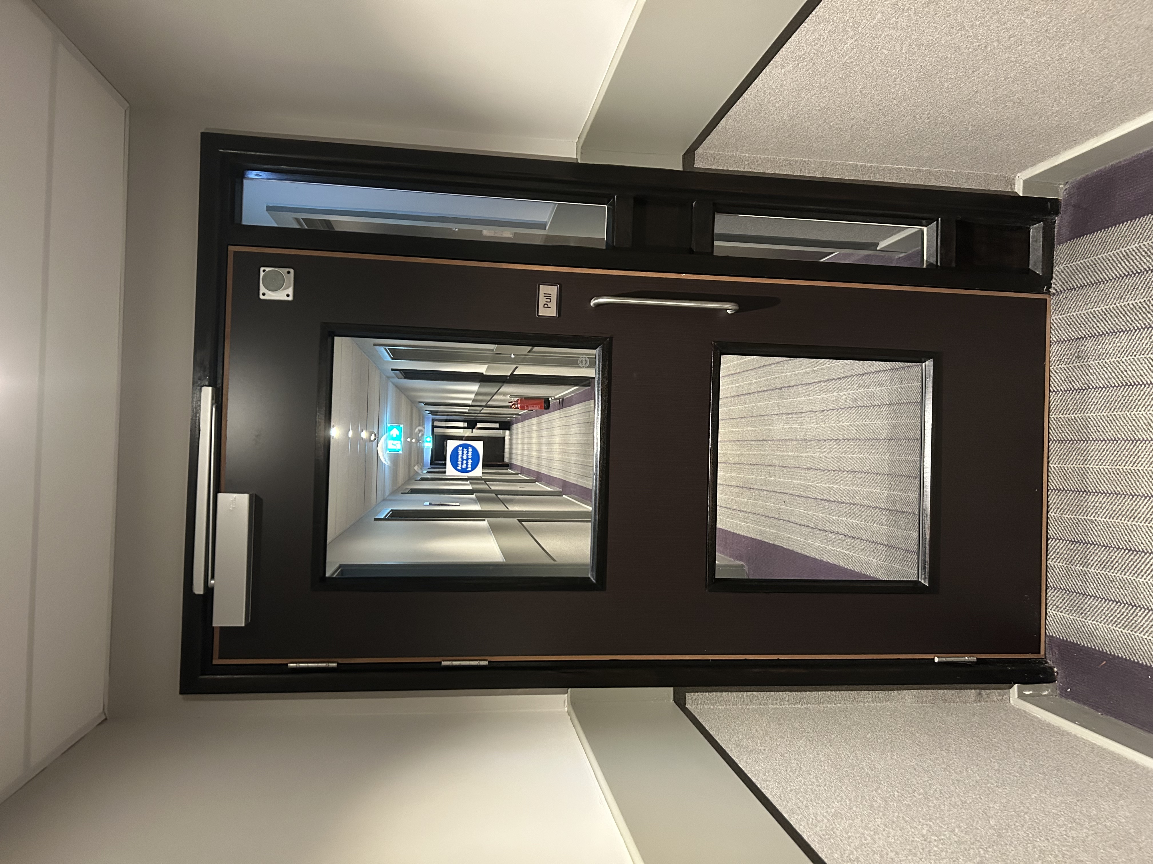Fire door with glazed vision panel and side screen in hotel corridor